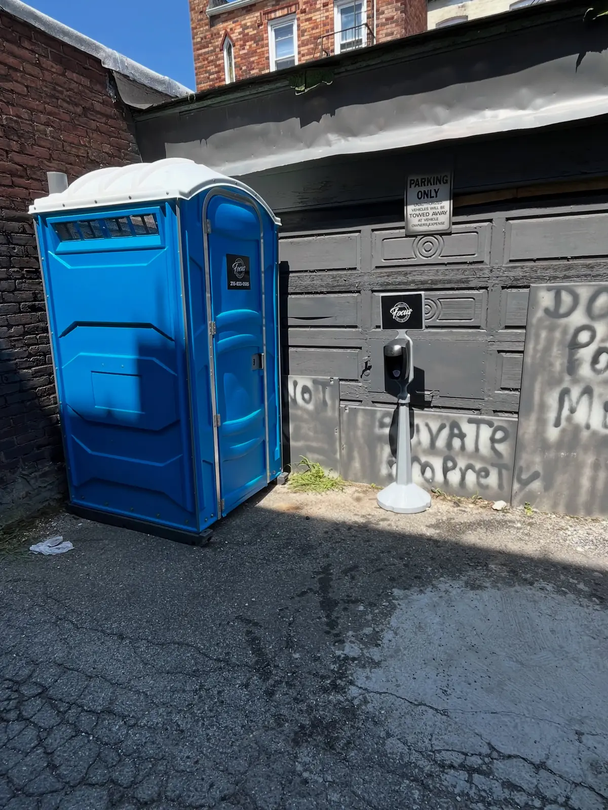 Standard porta potty placed beside a building on a narrow lot