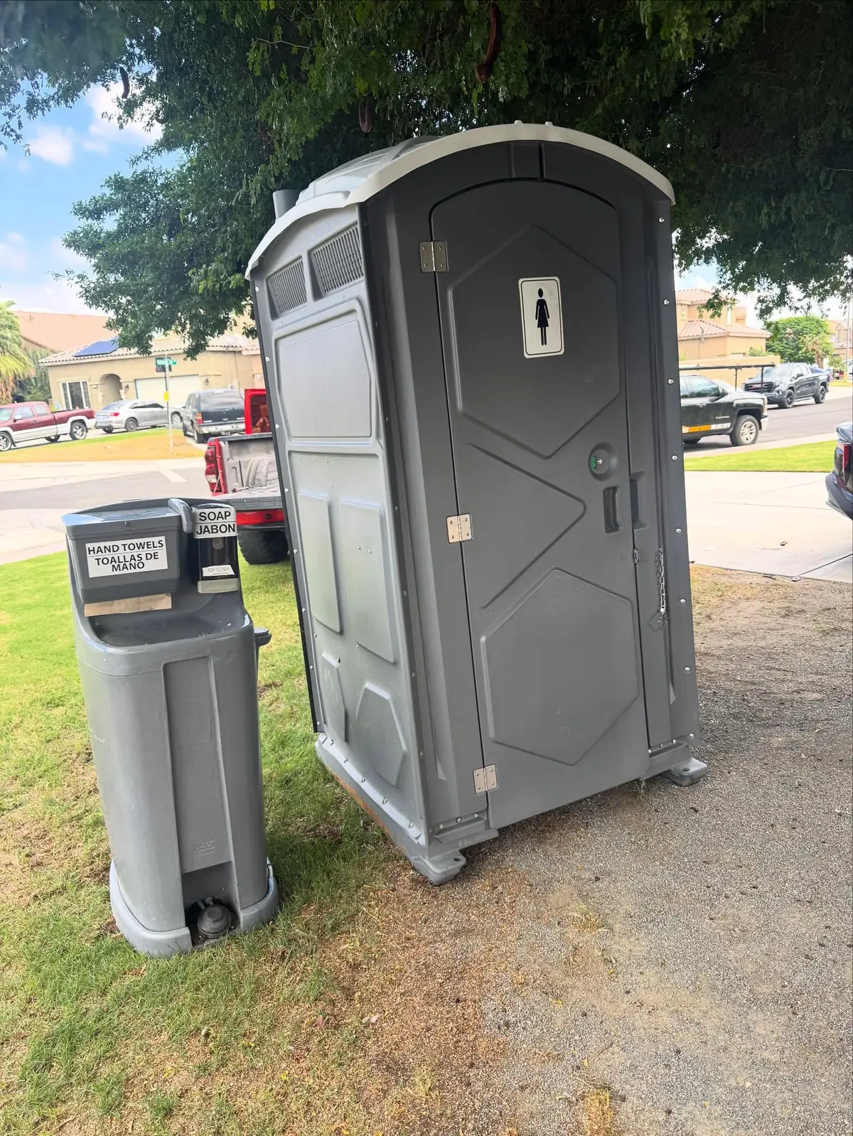Standard porta potty with a handwashing station on a lawn